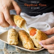 A plate of baked bread sticks with a pair of hands separating one stick in half showing melted cheese and pepperoni inside