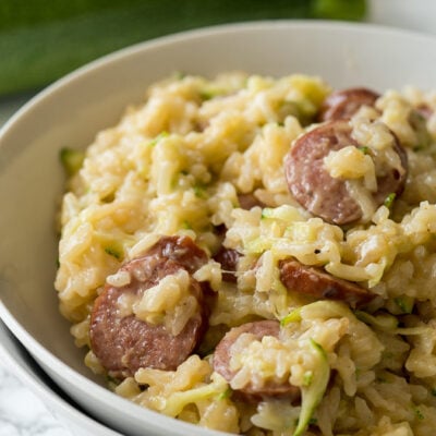 A close up of a plate of food, with sausage and zucchini rice