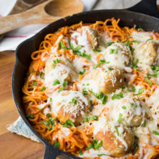 A skillet on a table, with meatballs, noodles, cheese and red sauce