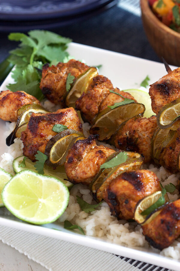 A plate with chicken chunks and lime slices on a skewers