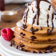 A plate with many stacked chocolate pancakes, topped with a scoop of ice cream, chocolate sauce and chocolate chips
