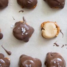 A sheet of Chocolate Covered Peanut Butter Pretzel Bites, with one peanut better topped pretzel not covered in melted chocolate