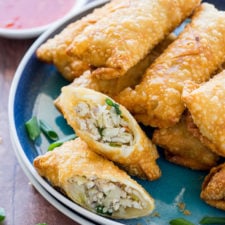 A plate of egg rolls, with one split in half in the front containing chicken
