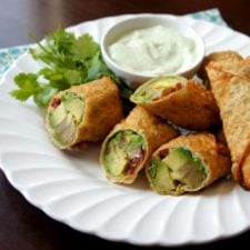 A plate with Avocado Egg Rolls on it next to a bowl of Creamy Cilantro Ranch Dip