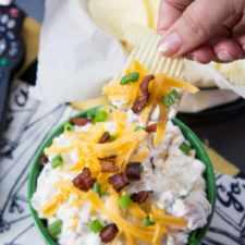 A close up a hand dipping a chip into Loaded Baked Potato Dip