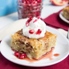 A piece of Pomegranate Pudding Cake drizzled in a sauce and topped with whipped cream and pomegranate