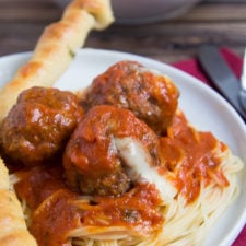 A plate with noodles topped with red sauce and cheesy meatballs