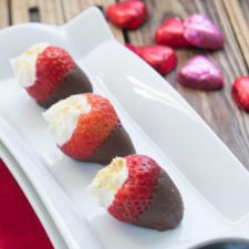 Three chocolate dipped strawberries on a plate stuffed with cheesecake