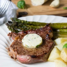 A close a plate with a steak and melting butter with a side of asparagus and potatoes