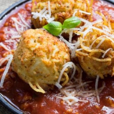 A close up of Spaghetti Balls topped with cheese on a plate of meat sauce