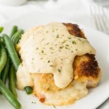 Food on a plate, with stuffed baked chicken with sauce on top and a side of green beans