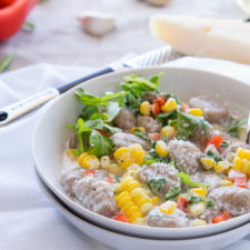 A bowl of food on a table, with cream sauce and veggies