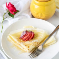 A plate of food on a table, with crepes toped with a sliced strawberry