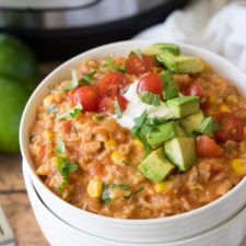 A bowl of food, with chicken, rice, corn and topped with slices of tomatoes, sour cream and avocado