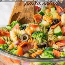 A bowl of pasta salad, with colorful curly pasta, olives, pepperoni, broccoli, cucumbers and tomatoes