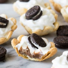 A close up of mini pie shells filled with a chocolate base, topped with whipped cream and a mini Oreo.