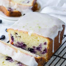 A slices of blueberry lime cake on a cooling rack, topped with drizzling frosting