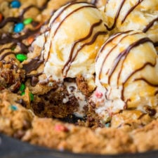 A close up of a large cookie with ice cream and syrup toppings