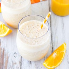 A glass of smoothie on a table, with orange and banana