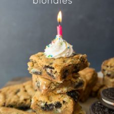 Squares of Oreo Birthday Cake Blondies topped with a dollop of white frosting with sprinkles and a lit candle
