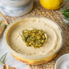 A container of food on a table, with Hummus and topping on top of it