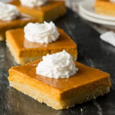 a close up of squares of pumpkin pie, topped with whipped cream