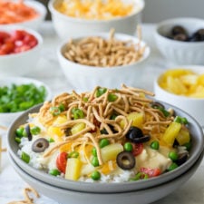 A close up fo a bowl food with rice, chicken sauce, veggies and other toppings