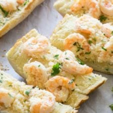 A close up of slices of a French loaf on a pan topped, with shrimp and herbs