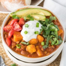 A bowl of chili, topped with sour cream, tomatoes, sweet potatoes, avocado and cilantro