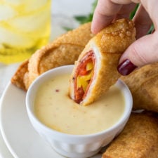 a plate of egg rolls with a bowl of dipping sauce, with one egg roll being dipped in the sauce