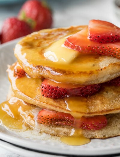 Stacked pancakes on a plate, with strawberries and topped with butter and syrup