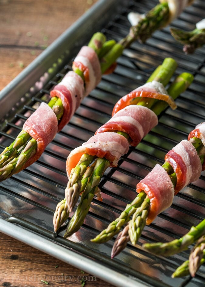 uncooked bacon wrapped around asparagus spears on cooking sheet.