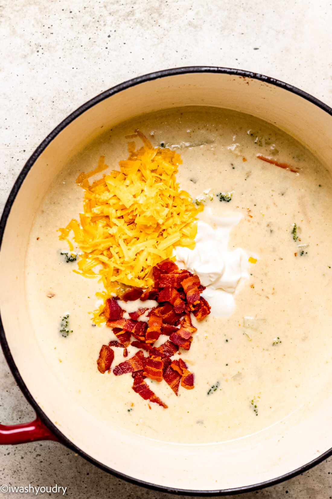 creamy soup in pot topped with cheese, sour cream and crumbled bacon.