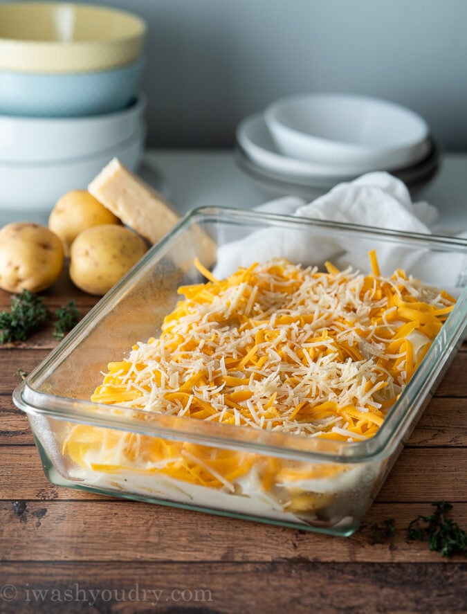 assembling scalloped potatoes in a casserole dish with cheese.