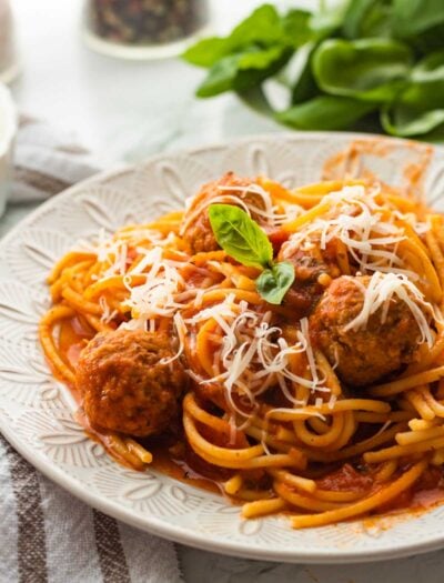 Cooked spaghetti with sauce and meatballs on white plate.