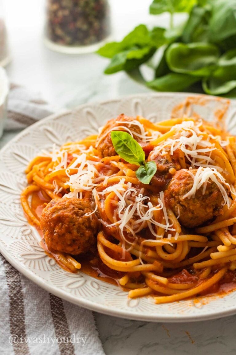 Cooked spaghetti with sauce and meatballs on white plate.