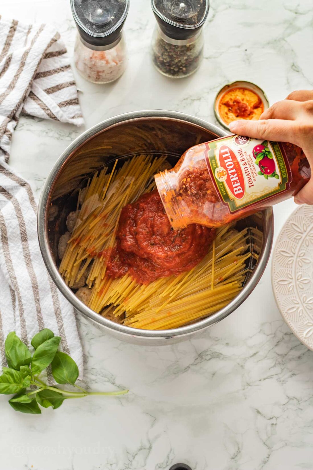 Pouring pasta sauce over uncooked spaghetti noodles in pot. 