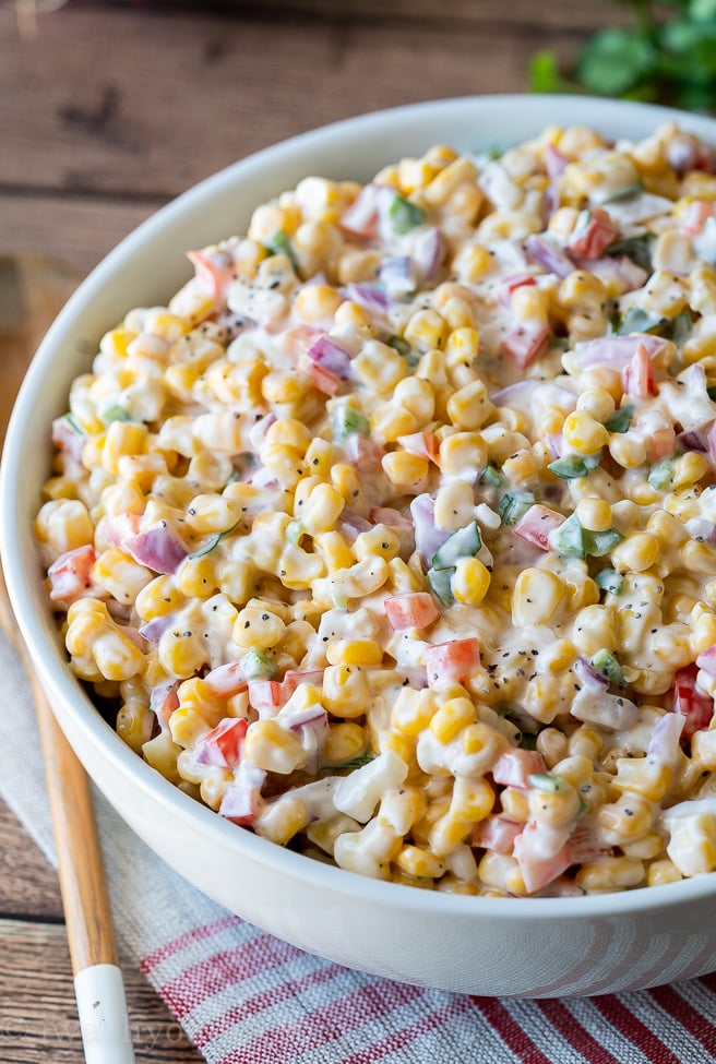 white bowl with creamy corn salad and red peppers.
