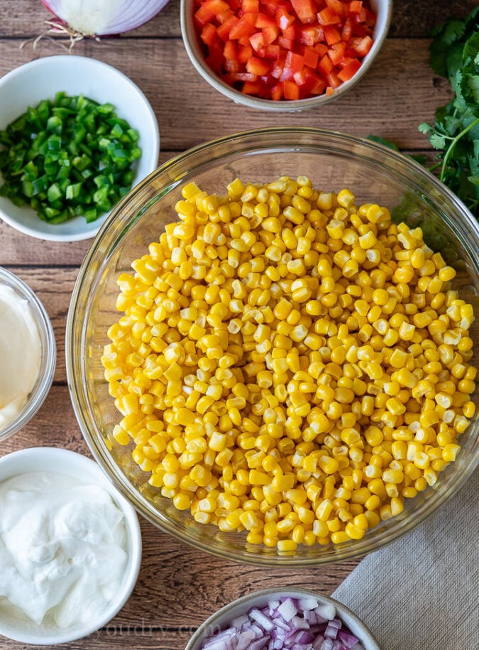 Corn salad ingredients in bowl on wooden surface.