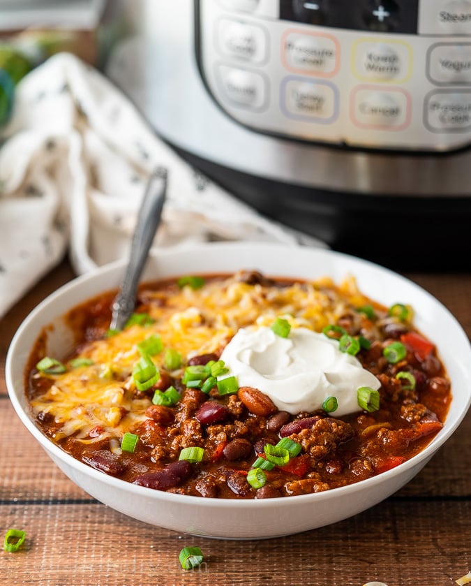 White bowl full of chili with cheese and sour cream on top.