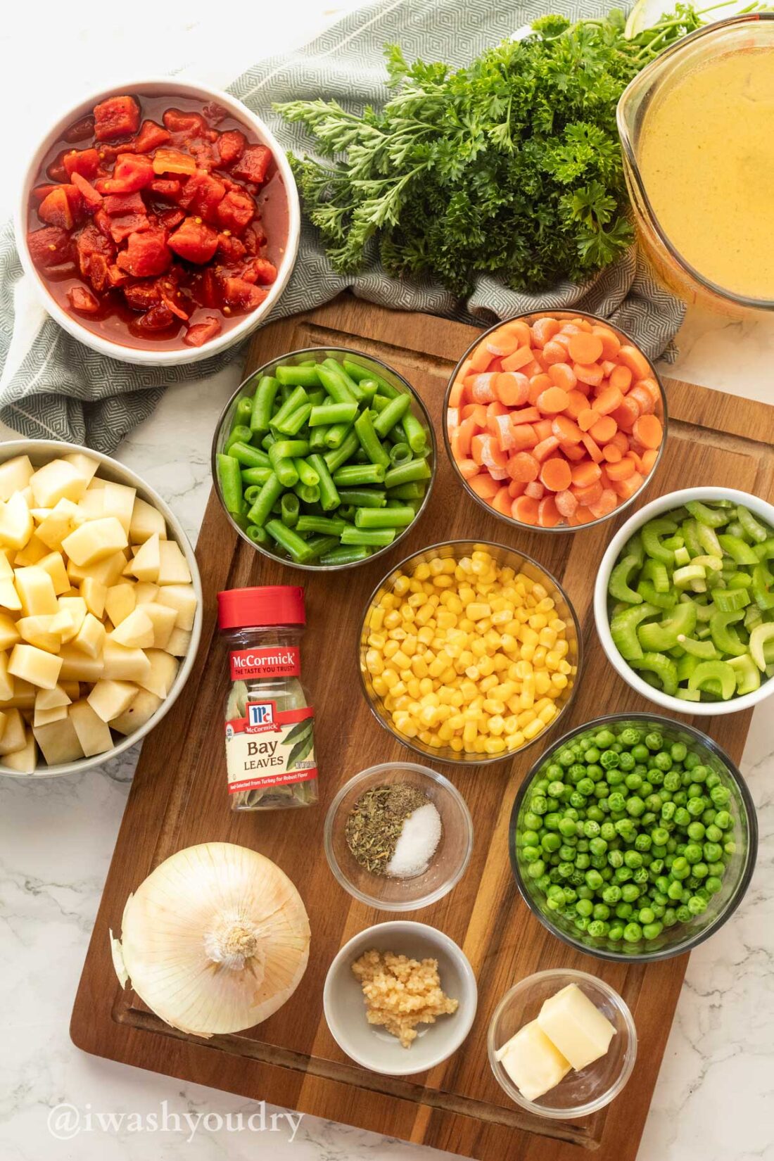 Ingredients for Vegetable Soup on white surface with cutting board.