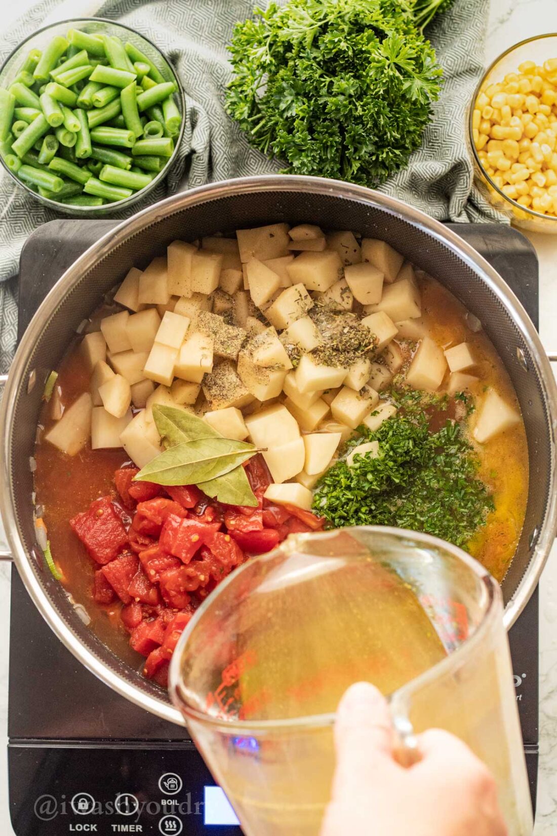 pouring broth in pot with potatoes and tomatoes.