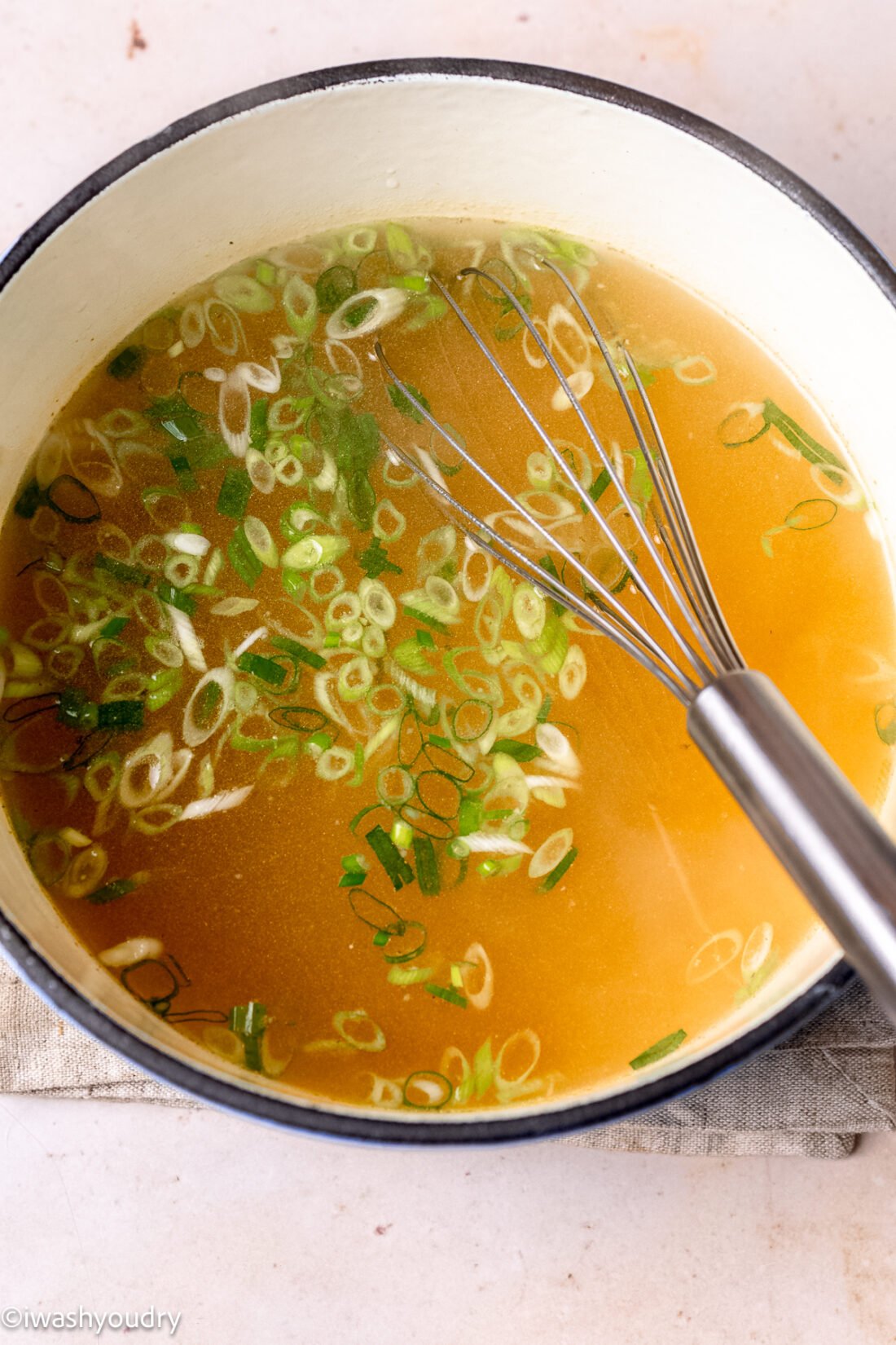 Broth with onions in metal pan with whisk. 