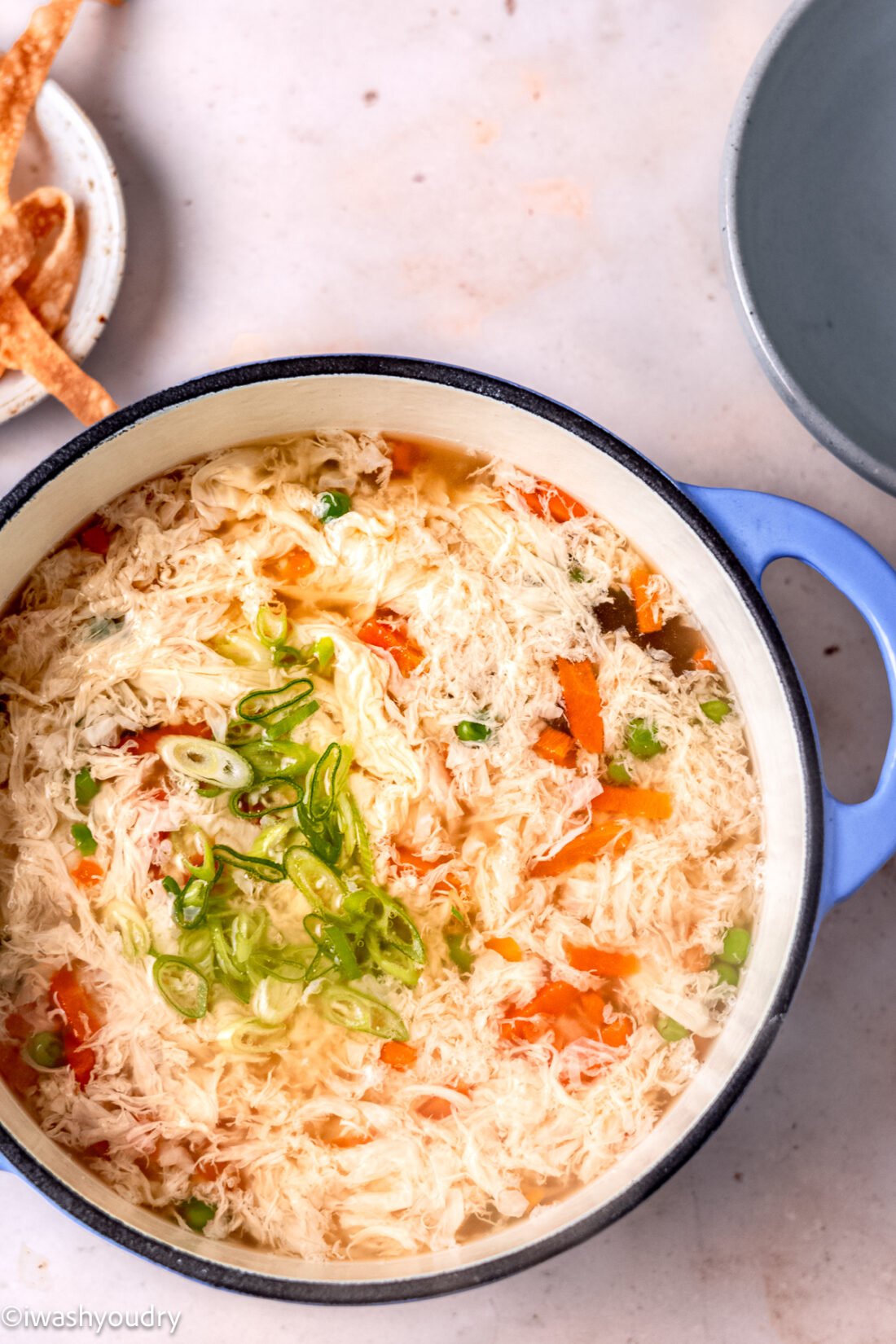 Cooked egg drop soup with carrots and green onions in pot. 