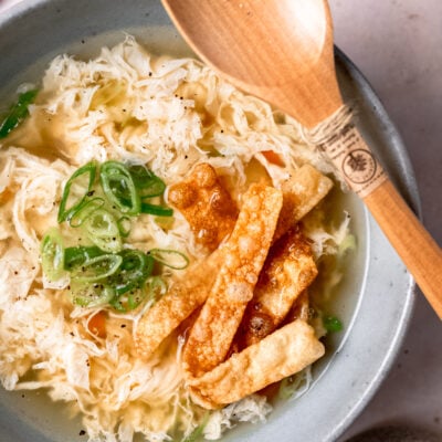 Cooked egg drop soup in gray bowl with wooden spoon.
