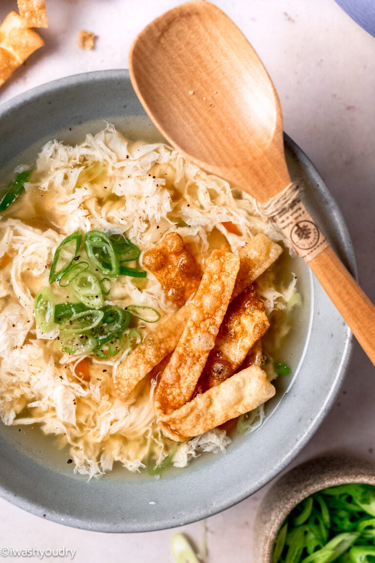Cooked egg drop soup in gray bowl with wooden spoon.