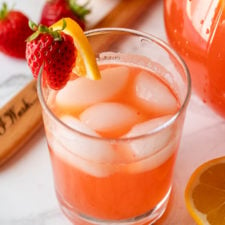 Clear glass full of strawberry lemonade with ice. Garnished with fresh strawberries and a lemon slice.