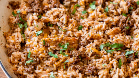 Close up shot of cheesy taco rice with bits of taco meat, gooey cheese and fresh cilantro on top.