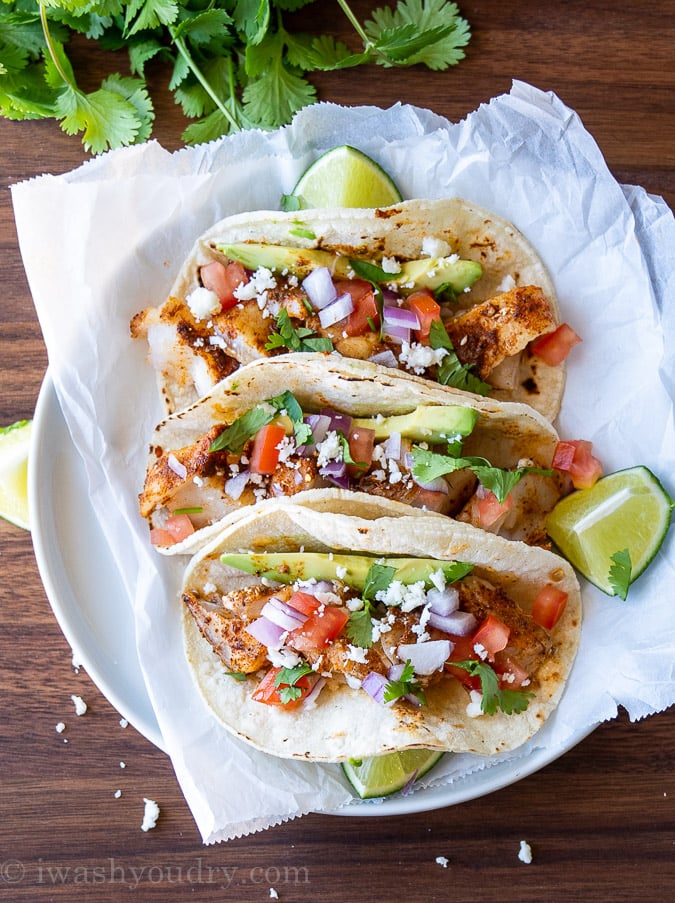 Top down image of three fish tacos on a plate with lime wedges beside them.