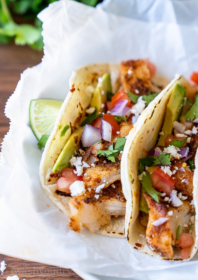 Close up picture of a fish taco topped with fresh pico de gallo and avocado slice.